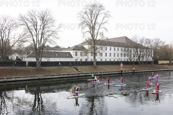 Water sports enthusiasts dressed up as Santa Claus ride SUPs on the Spree in front of Bellevue