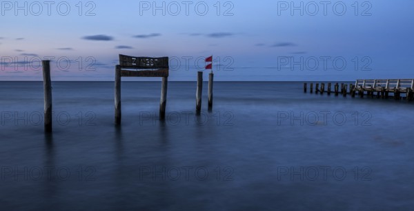 Wooden sign in the sea with inscription Zingst and wooden walkway, long exposure, evening light,