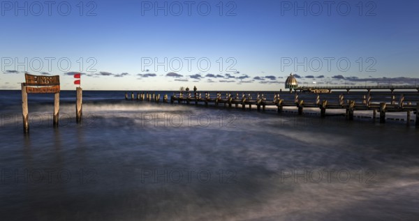 Wooden sign in the sea with inscription Zingst and wooden walkway, pier with diving gondola behind,