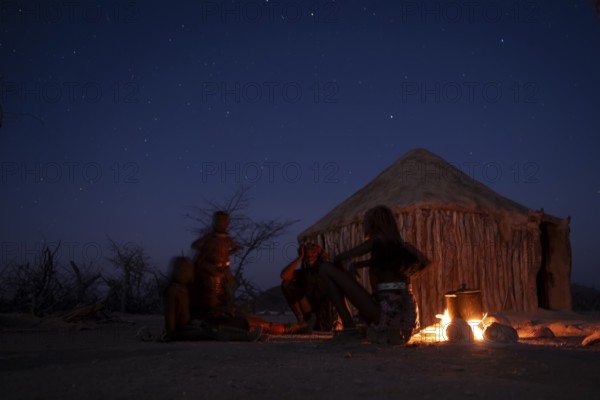 Himba at the campfire in the evening, night view, Himba huts, traditional Himba village in the