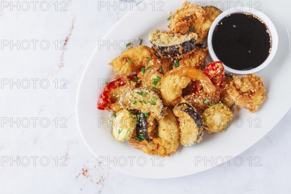 Shrimp and assorted vegetables are deep fried in a light batter and served on a white plate. A