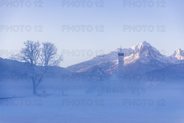 Snowy mountain landscape with St. Coloman pilgrimage church in the foreground and foggy background,