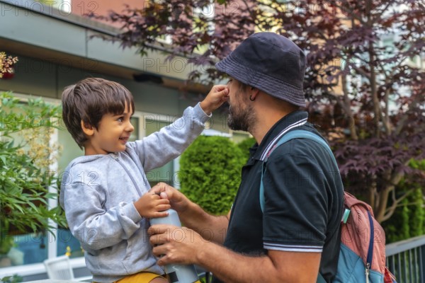 Playful preschool child touching his father's nose while holding a water bottle in a residential