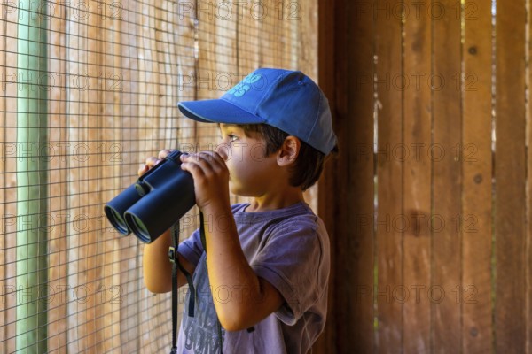 Young boy wearing a blue cap observing wildlife through binoculars at a nature park in kamloops,