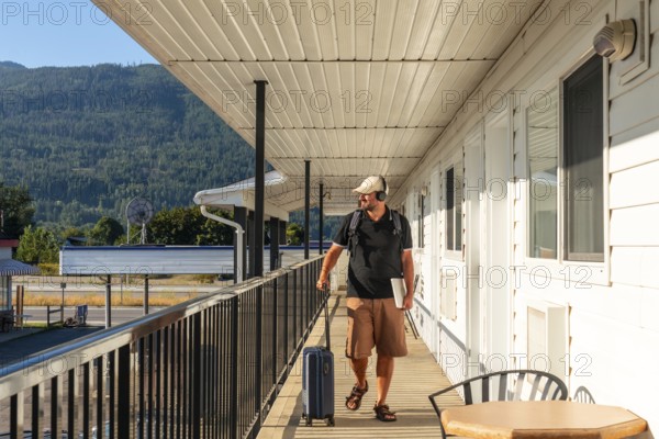 Digital nomad walking along a motel balcony, surrounded by luggage and a laptop, soaking in the