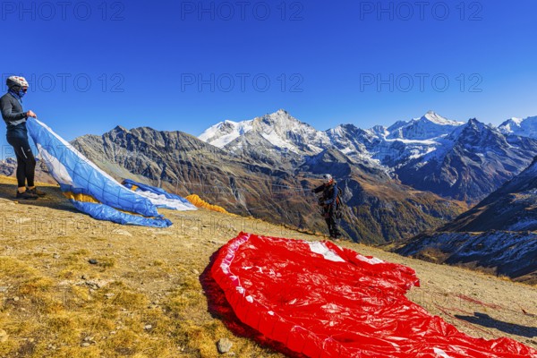 Paragliders are preparing for their start, with the snow-capped peaks of the Valais Alps, Val