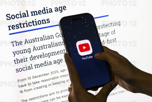 In this photo illustration, a person holds a phone displaying the YouTube app in front of a screen
