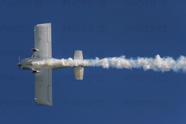 Stunt aerobatic plane performing stunts in blue sky with smoke trail. Concept of speed, difficulty,