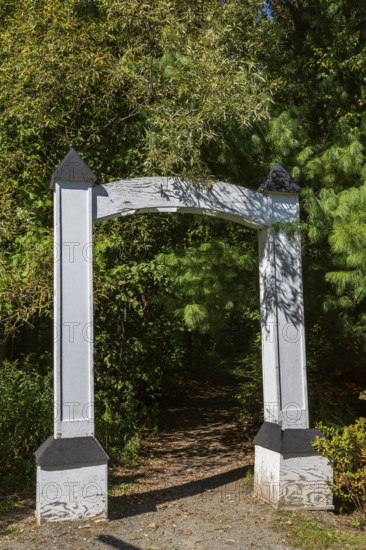 White painted wooden portal gate at start of hiking trail in public nature park in late summer,