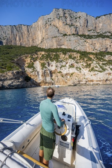 Young man rides a motorboat along the picturesque rocky coast, cliffs and blue sea, Golfo di