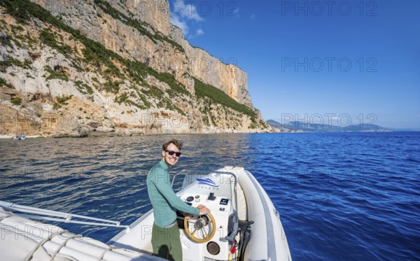 Young man rides a motorboat along the picturesque rocky coast, cliffs and blue sea, Golfo di