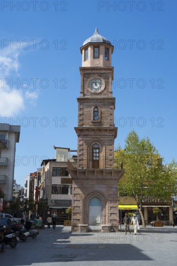 A tall clock tower in an urban square with trees and shops, Çanakkale Clock Tower, Canakkale,