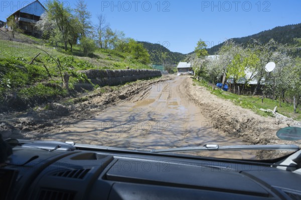 A muddy country road is viewed from a driving perspective through a car window, campers on a