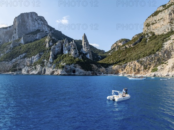 Couple on motorboat off picturesque rocky coast, cliffs with L'Aguglia pinnacle, blue sea and Cala