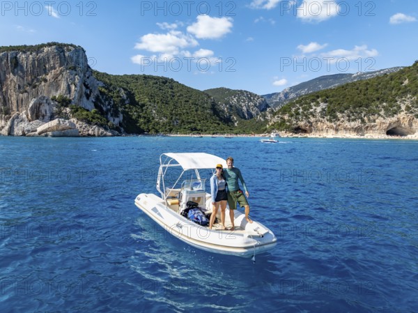Couple, young woman and young man on motor boat off picturesque rocky coast, cliffs and Cala Luna