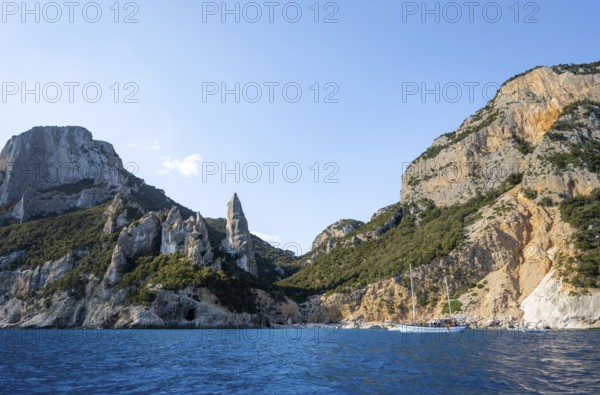 Excursion boat off picturesque rocky coast, cliffs in morning light, L'Aguglia pinnacle, blue sea