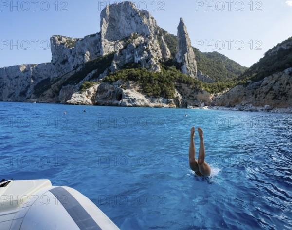 Young woman jumping from a boat into the water, picturesque rocky coast, cliffs with L'Aguglia rock
