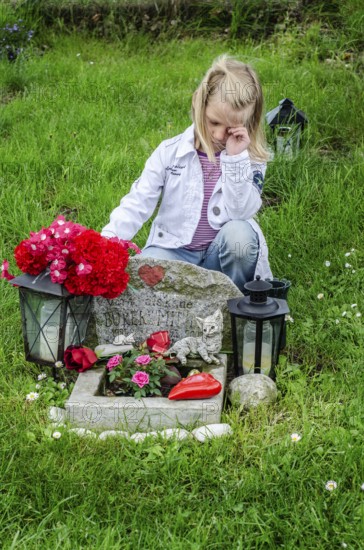 Grieving blonde 7-year-old girl at her cat's grave at pet cemetery in Ystad, Skåne County, Sweden,