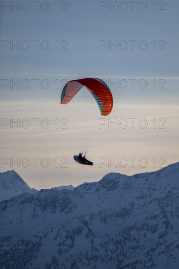 Paragliders flying over snowy mountain peaks in winter in evening light, Kitzbühel Alps, Tyrol,