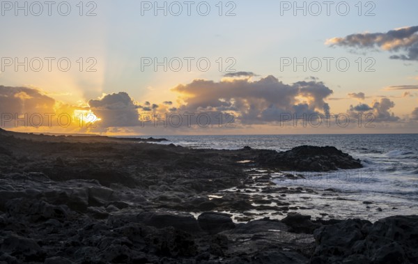 Dramatic cloudy sky with sunbeams at sunset, seaside coast with volcanic rocks, La Santa,