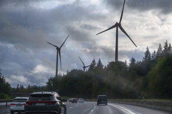 Tourist traffic on the A9 motorway during thunderstorms, wind turbines in the pine forest in the
