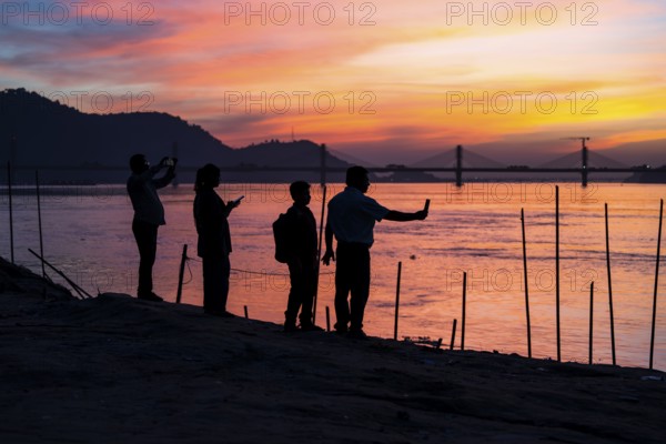 People enjoy the vibrant sunset by the Brahmaputra riverside, capturing photos and moments against