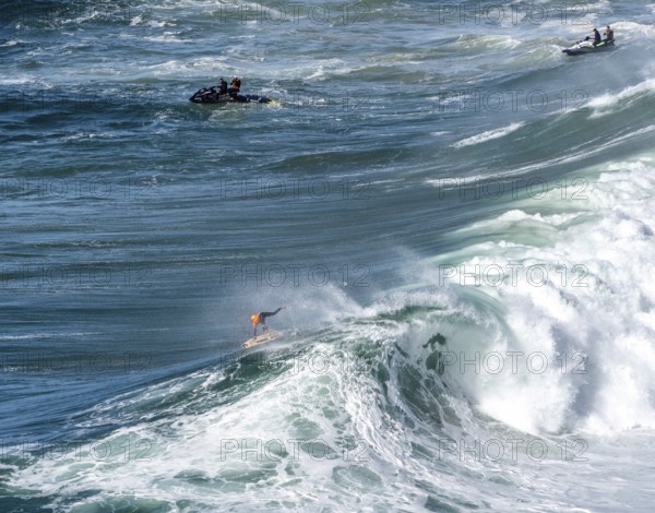 Surfers with their jet ski pilots in the Atlantic waves below Farol de Nazaré, Forte São Miguel,