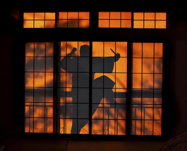 Shadow of a man, burglar with knife, assassin, ninja, on the balcony behind sliding shoji doors in