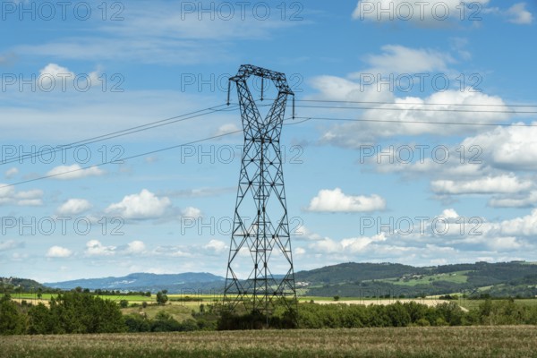 High voltage power lines against a bright blue sky with scattered clouds, Puy de Dome, Auvergne