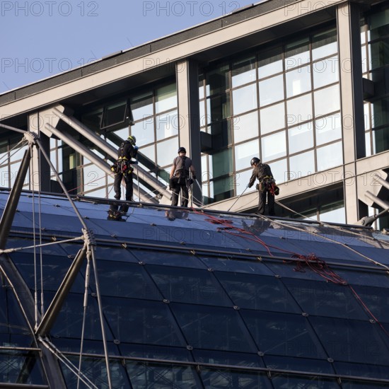Three male glass cleaners abseiling down a glass roof of Berlin Central Station to clean windows,