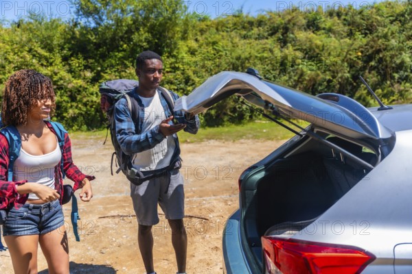 Young couple of hikers preparing their backpacks for an exciting road trip, opening the car trunk