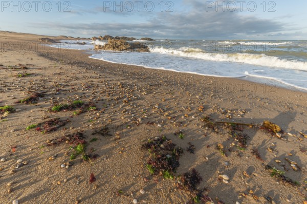 The waves crash gently against a rocky shoreline at sunset, creating a tranquil atmosphere. The