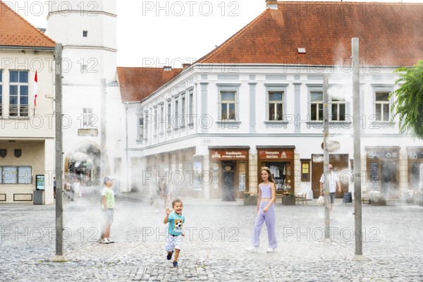 Water mist system in the city centre of Trencin, children use the refreshment in the summer heat,
