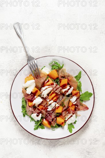 Salad with slices of ripe melon, prosciutto, mozzarella and fresh arugula, decorated with balsamic