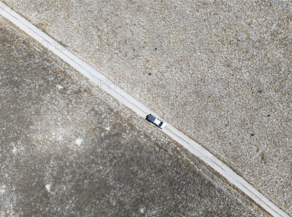 Off-road vehicle driving on a sandy track through a vast dry landscape with yellow grass, Top Down,
