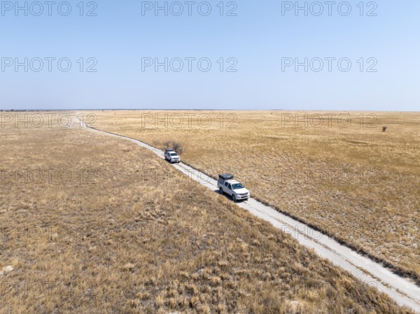 Two off-road vehicles drive on a sandy track through a vast dry landscape with yellow grass, Sowa