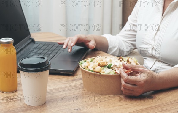 A woman is working on a laptop at home, there is food on the table, salad, coffee and juice,
