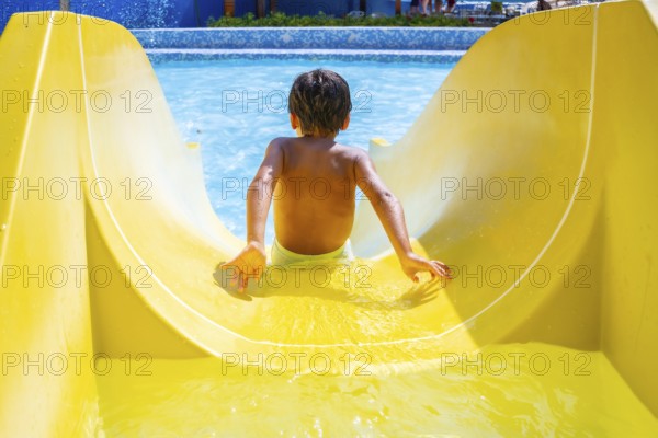 Boy joyfully sliding down a colorful waterslide in an aquapark, enjoying summer vacation with