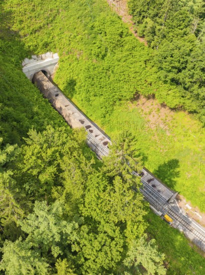 A train disappears into a tunnel, surrounded by forest in a bird's eye view, construction of the