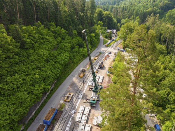 Construction work with a crane along railway tracks, surrounded by forest, construction of the