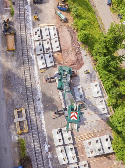 Industrial site with crane, concrete blocks and railway tracks surrounded by trees from an aerial
