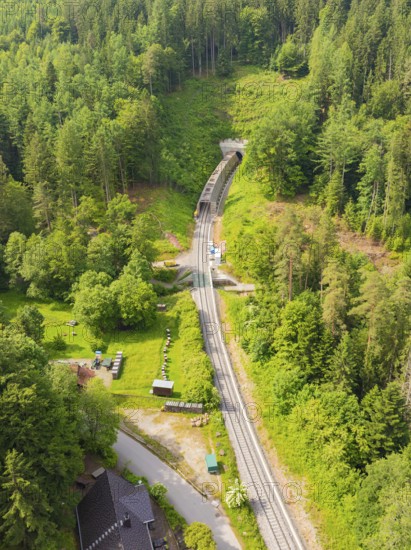 Aerial view of a railway tunnel running through a green, wooded landscape, construction of the
