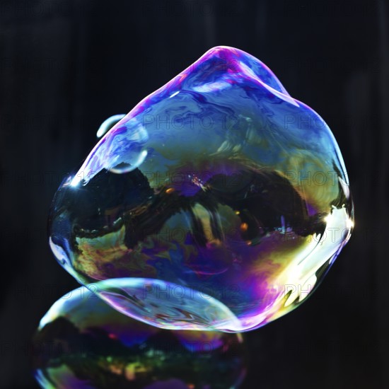 Large, irregular, iridescent soap bubbles in the colours of the rainbow against a black background,