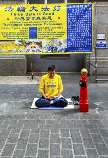 Falun Dafa or Falun Gong man meditating sitting cross legged, Gerrard Street, Chinatown, West End,