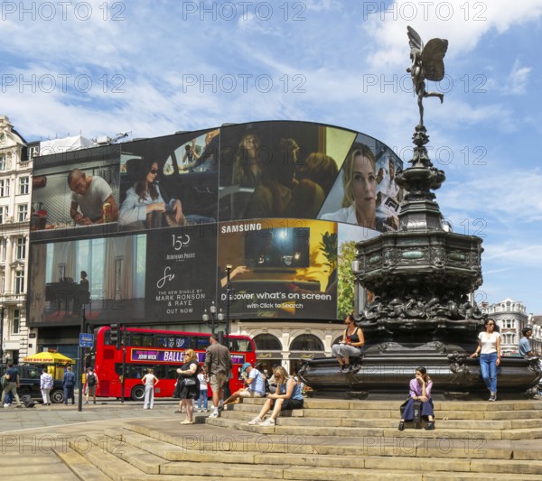 People sitting around Eros statue, Piccadilly Circus, central London, England, UK - Shaftesbury