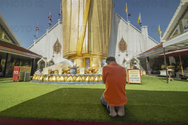 Man praying in front of a 32 metre high standing Buddha decorated with glass mosaics and 24 carat