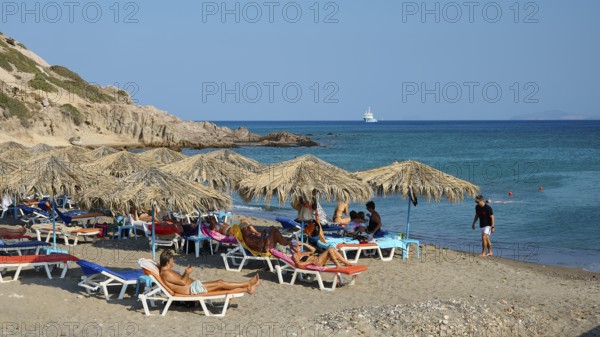 Beach scene with deckchairs and beach mats under umbrellas near the sea, Agios Stefanos Beach,