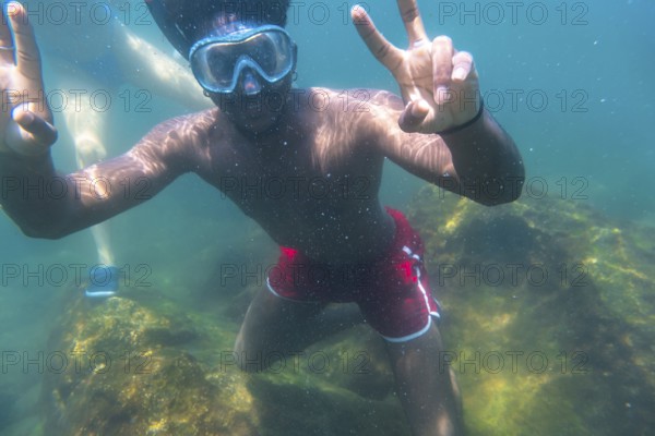 Young man snorkeling underwater, flashing the peace sign with both hands, enjoying the vibrant blue