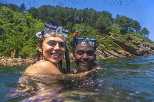 Interracial couple enjoying snorkeling adventure, embracing in refreshing ocean waters with scenic