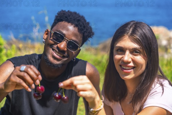 Interracial couple smiling while sharing fresh cherries, enjoying a sunny summer vacation by the
